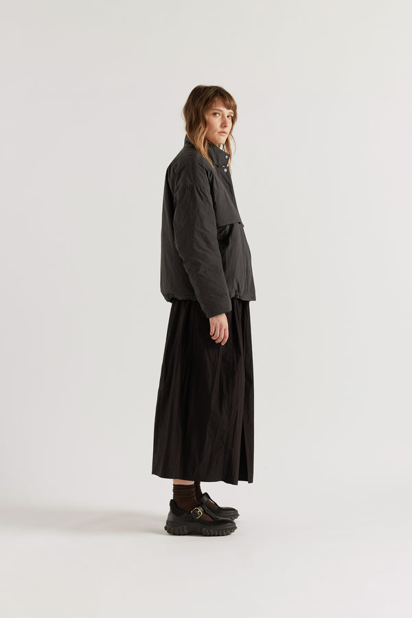 Side of female model in the black Surge Quilted Jacket worn closed, showing relaxed silhouette, military tab collar and storm flap pocket detailing