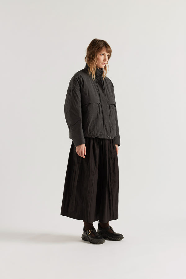 Front of female model in the black Surge Quilted Jacket worn closed, showing relaxed silhouette, military tab collar and storm flap pocket detailing