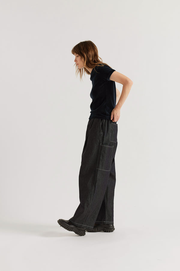 Side profile of loose-fit dark indigo cargo pants showing wide cargo-pocket detailing and relaxed proportions.