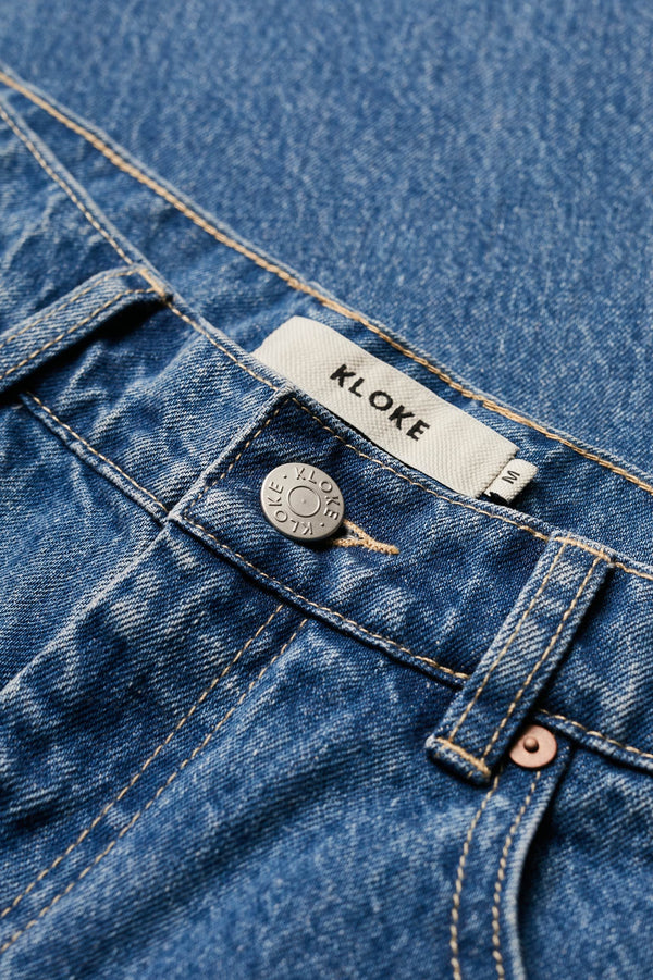 Close up details of The sworn denim jean in Mid Wash Blue. Looser fit all-purpose jeans in premium Japanese denim with zip fly, button closure, five-pocket design, and Kloke branded hardware. Available in 8 sizes.