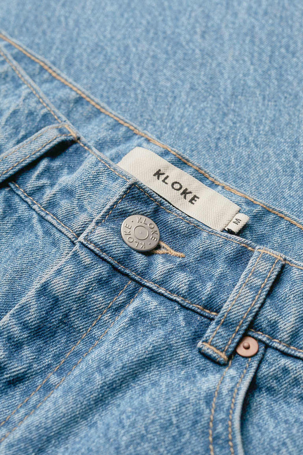 Close up details of The sworn denim jean in Pale Wash Blue. Looser fit all-purpose jeans in premium Japanese denim with zip fly, button closure, five-pocket design, and Kloke branded hardware. Available in 8 sizes.